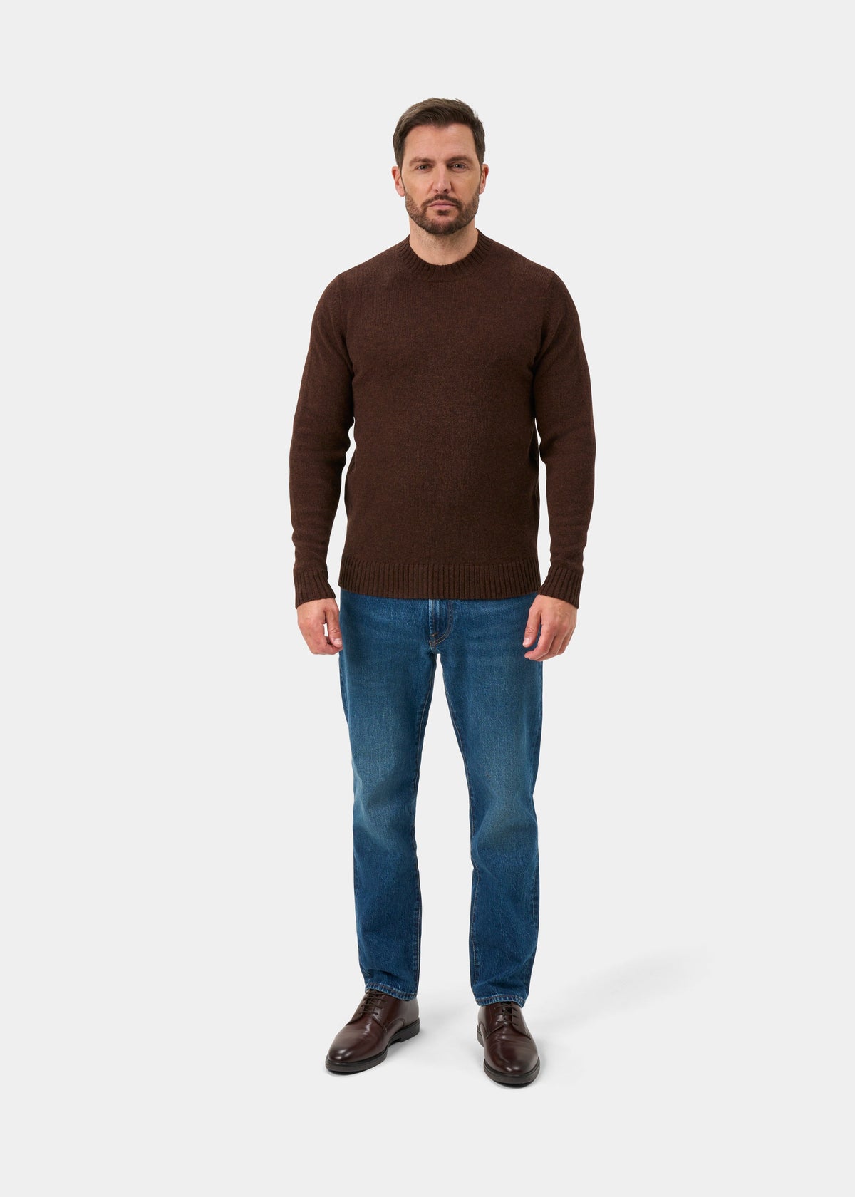 Man in Kinnadie Supersoft Shetland Wool Crew Neck Jumper in Coffee, blue jeans, and brown shoes on white background.
