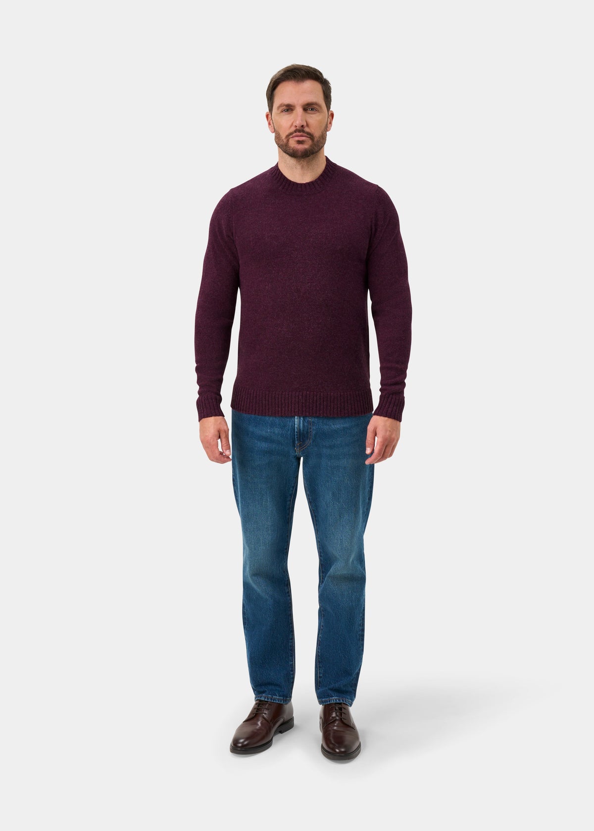 Man facing forward in the Kinnadie Supersoft Shetland Wool Crew Neck Jumper in Elderberry, blue jeans, brown shoes.