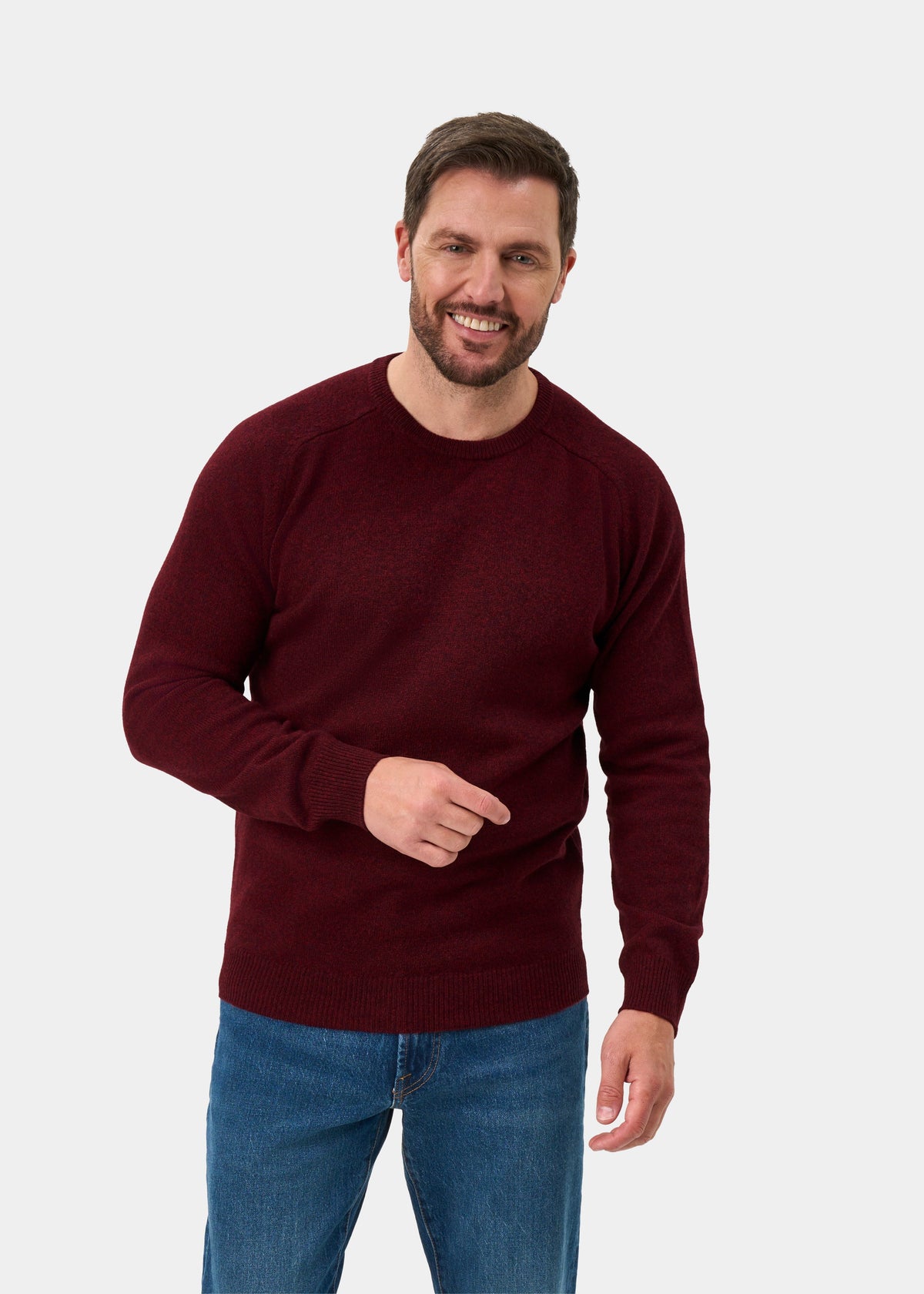 Man wears Lenzie Lambswool Crew Neck Jumper in Red Velvet, smiling and gesturing against a light background.